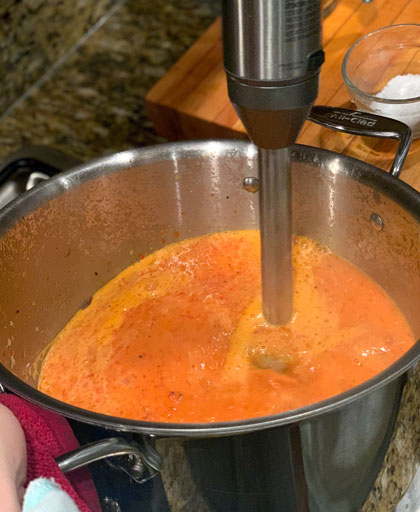 roasted red pepper, onions, garlic and vegetable broth being mixed with a hand mixer.
