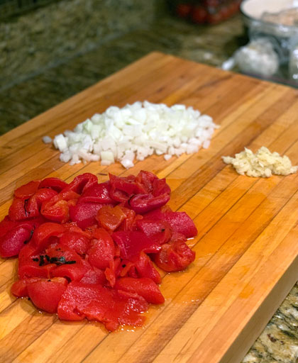 roasted red pepper, onion and garlic chopped on a cutting board.